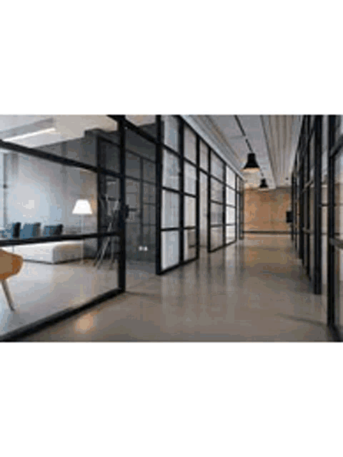 a long hallway in a modern office building with glass walls and a couch .