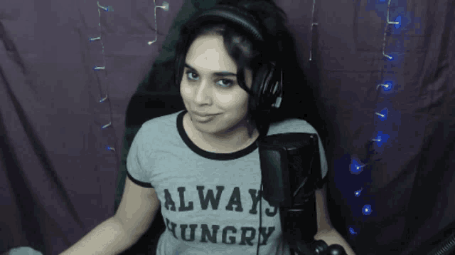 a woman wearing headphones and a grey shirt that says always hungry