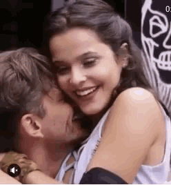 a man and a woman are hugging each other and smiling . the woman is kissing the man on the cheek .
