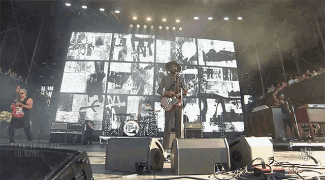 a man playing a guitar on a stage with a large screen behind him that says ' nc '