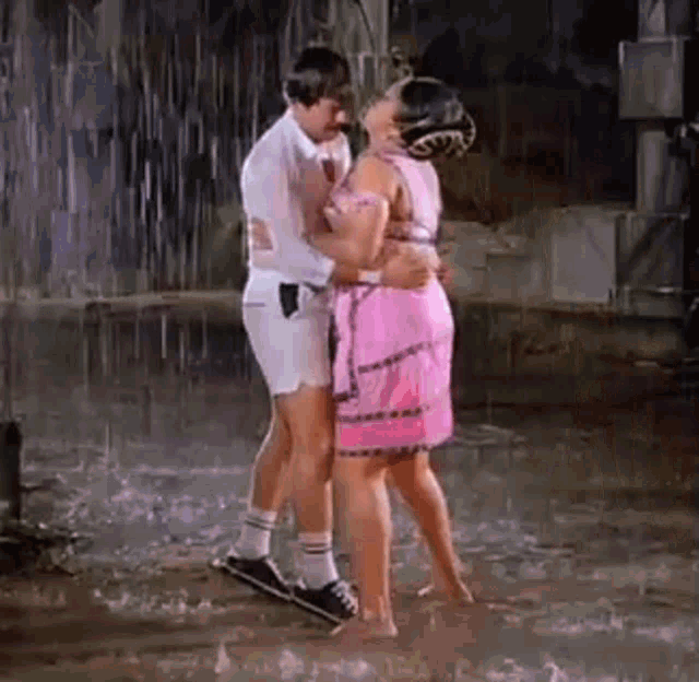 a man and a woman are dancing in the rain . the woman is wearing a pink dress .