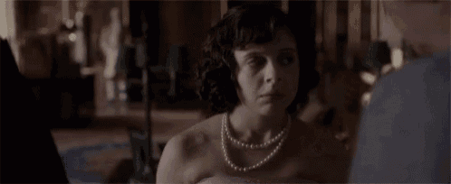 a woman wearing a pink dress and a pearl necklace is looking at a man .