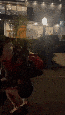 a group of people are standing on the side of the road in front of a building at night .