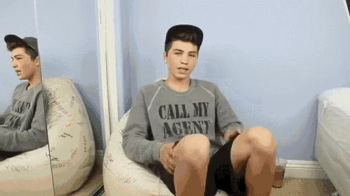 a boy wearing a sweatshirt that says call my agent sits on a bean bag chair