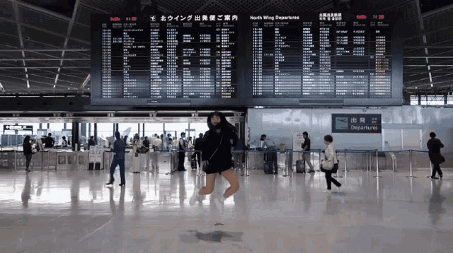 a woman stands in front of a departures board at an airport