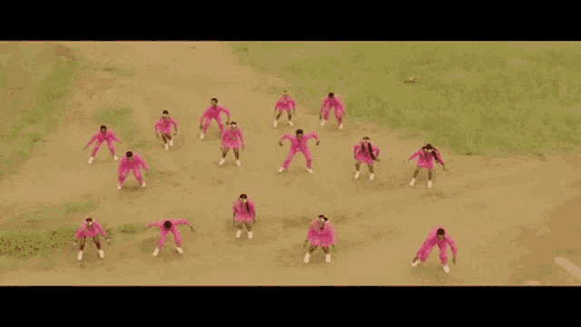 a group of people in pink uniforms are dancing on a dirt road .