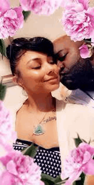 a man and a woman are kissing in front of pink flowers .