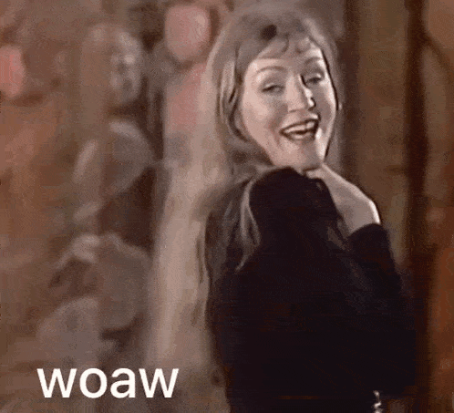a woman in a black dress is smiling and dancing in a room with the words wow written on the bottom .