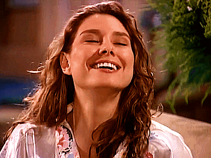 a woman is smiling with her eyes closed and her hair is blowing in the wind