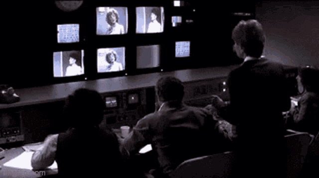 a group of people are sitting in front of a bunch of television screens
