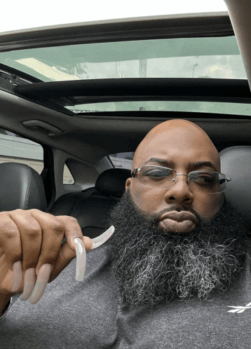 a man with a beard and long nails is sitting in a car with the sunroof open