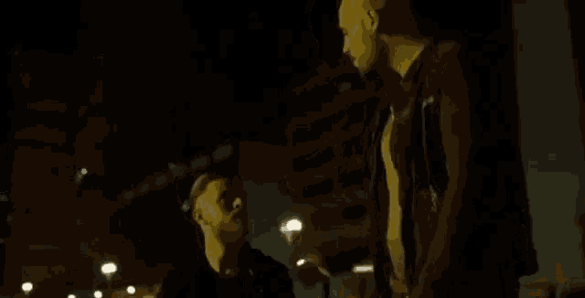 two men are standing next to each other in the dark and one of them is touching the other 's face .
