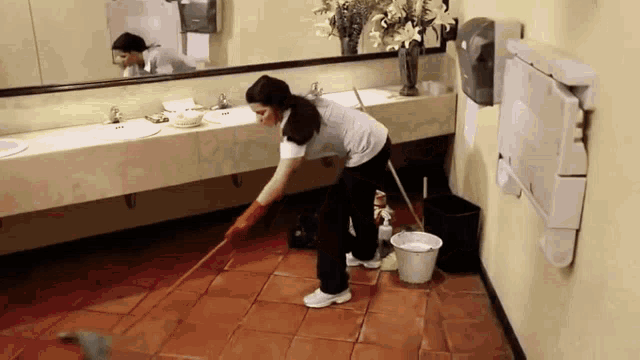 a woman is mopping the floor in a public restroom