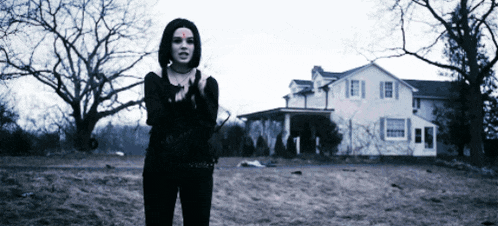 a woman in a black outfit stands in front of a large white house