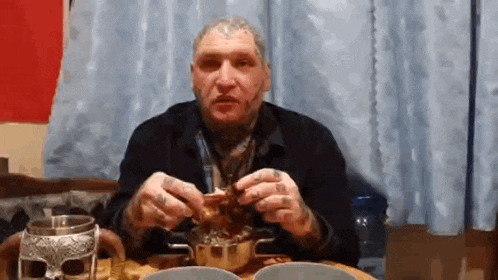 a man with a tattoo on his face is sitting at a table eating .