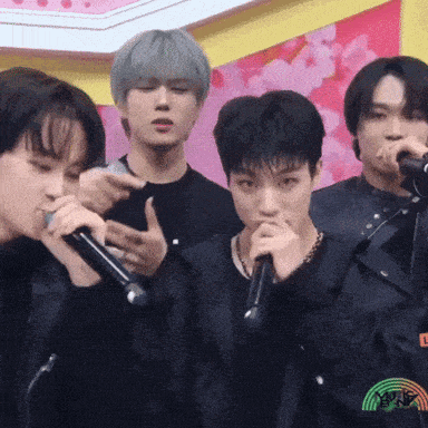 a group of young men are singing into microphones with a rainbow in the background
