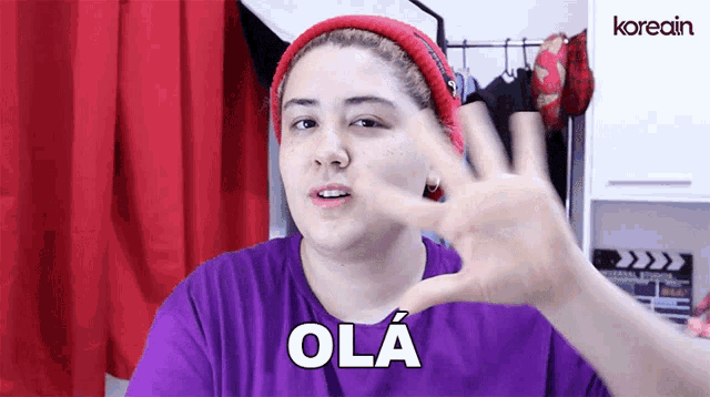 a woman wearing a red beanie and a purple shirt says " ola "