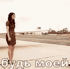 a woman in a dress is standing on a sidewalk with the words " будь моей " on the ground