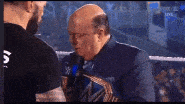 a man in a suit is talking into a microphone while wearing a wrestling belt with the w logo on it