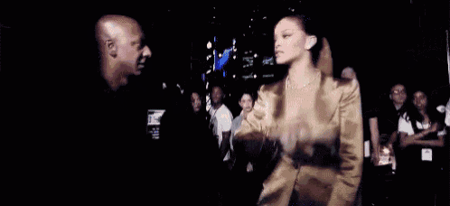 a woman in a gold jacket is standing in a crowd of people in a dark room .