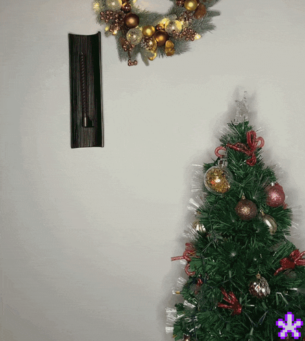 a green christmas tree with red and gold ornaments and a wreath behind it