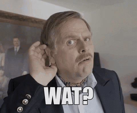 a man in a suit and tie is holding his hand to his ear and says wat .