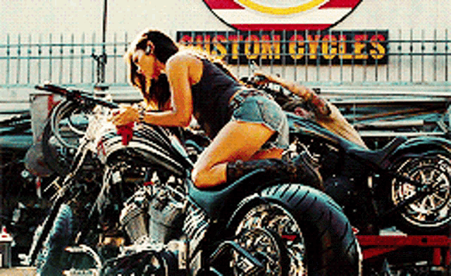 a woman kneeling on a motorcycle in front of a custom cycles sign