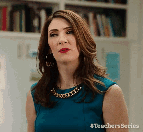 a woman wearing a blue dress and a gold chain around her neck is standing in front of a bookshelf .