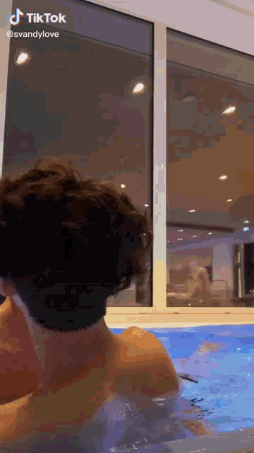 a man without a shirt is swimming in a pool with a window in the background .
