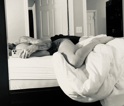 a person with a tattoo on their arm laying on a bed taking a picture