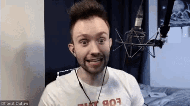 a man with a beard is wearing a white t-shirt and headphones in front of a microphone and smiling .
