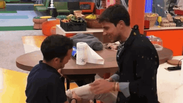two men are sitting at a table with a roll of paper towels on it