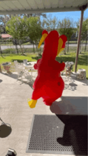 a red stuffed animal with yellow wings is standing on a porch .