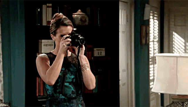 a woman is taking a picture with a camera in front of a bookshelf with a number 12 on it