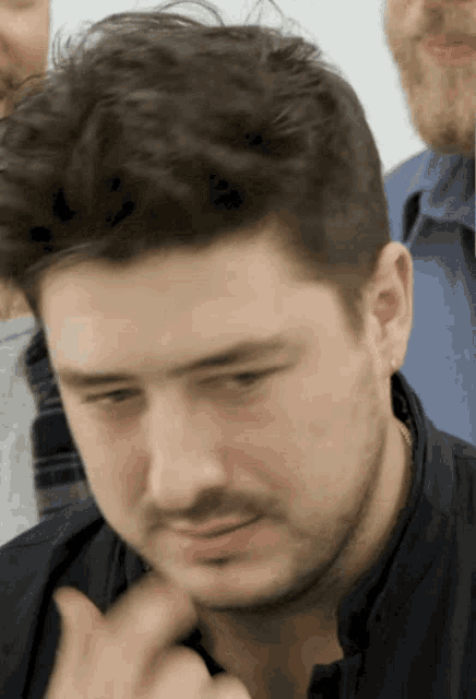 a man with a beard and ear piercings looks at the camera