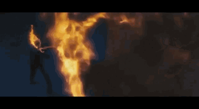 a man is standing in front of a large fire with a torch in his hand .