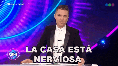 a man in a tuxedo stands in front of a sign that says " la casa esta nerviosa "