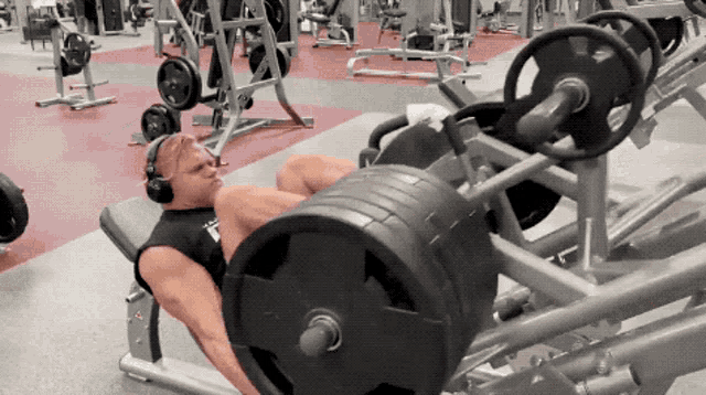 a man wearing headphones is squatting on a machine in a gym