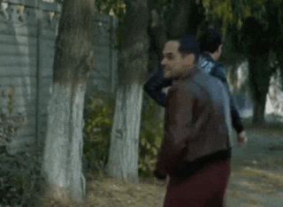 a man in a leather jacket is walking down a sidewalk next to trees .