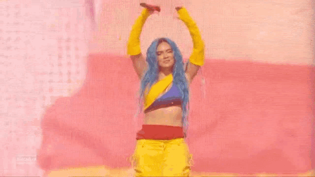 a woman with blue hair and yellow gloves is dancing on a stage with a microphone .