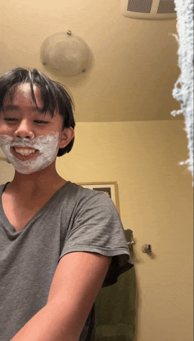 a young man with shaving cream on his face smiles in front of a mirror