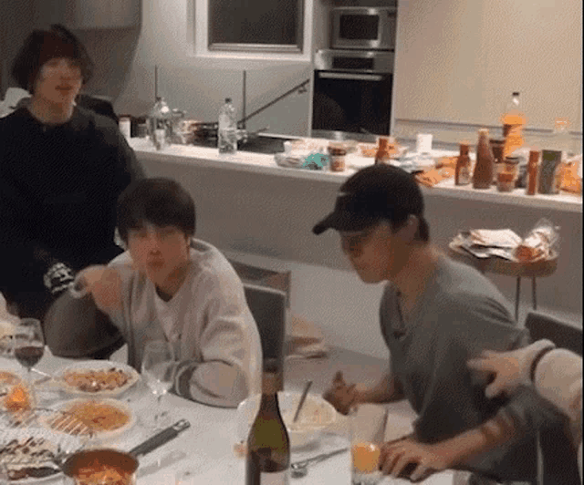 a group of people are sitting at a table in a kitchen eating food .