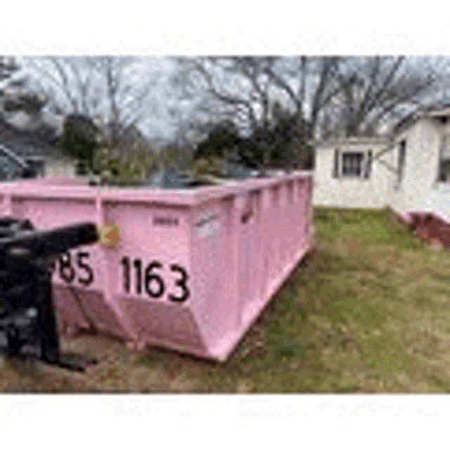 a pink dumpster is parked in front of a house in a yard .
