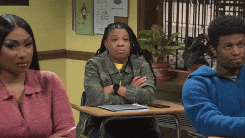 a woman sits at a desk with her arms crossed while a man sits in a blue sweatshirt