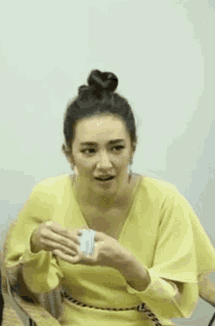 a woman in a yellow dress is sitting in a chair holding a piece of paper and making a funny face .