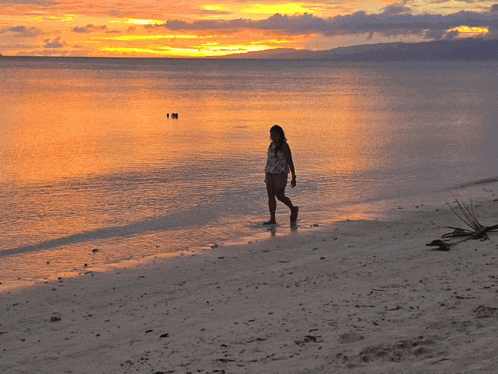 a woman walks along the beach at sunset