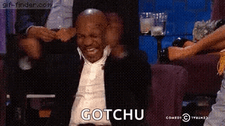 a man in a suit is sitting on a couch with his arms outstretched and the word gotchu written on the screen .