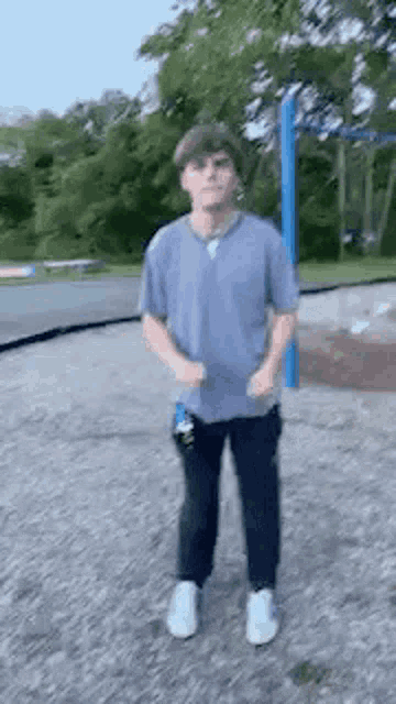 a man in a blue shirt and black pants is standing in a park .
