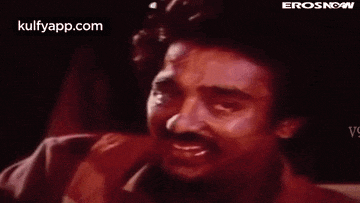a man with a mustache is crying and smiling in a dark room .