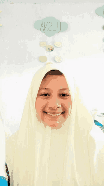 a girl wearing a white hijab smiles in front of a sign that says avizun